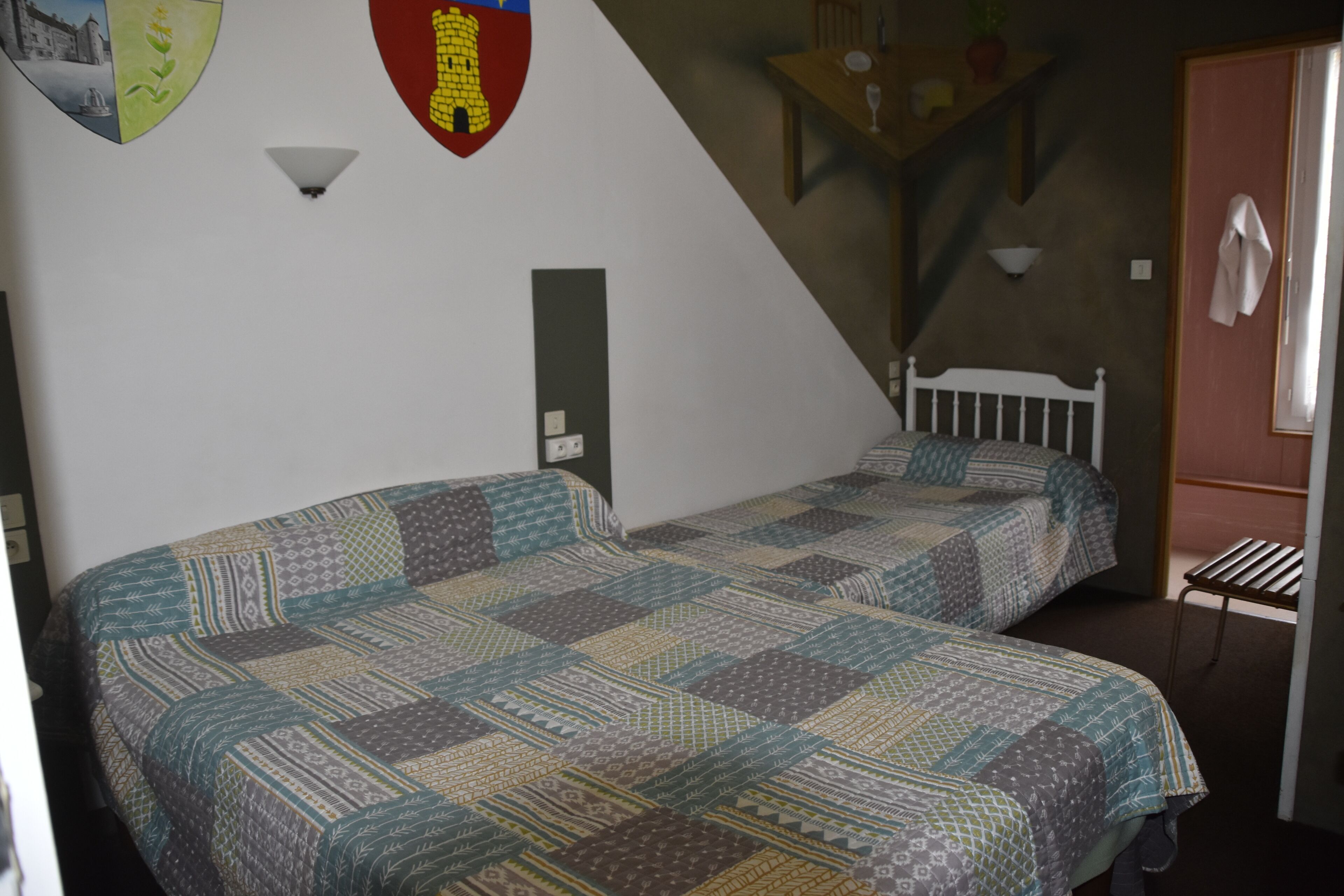A room with two beds, a wall-mounted light fixture, and a coat rack.