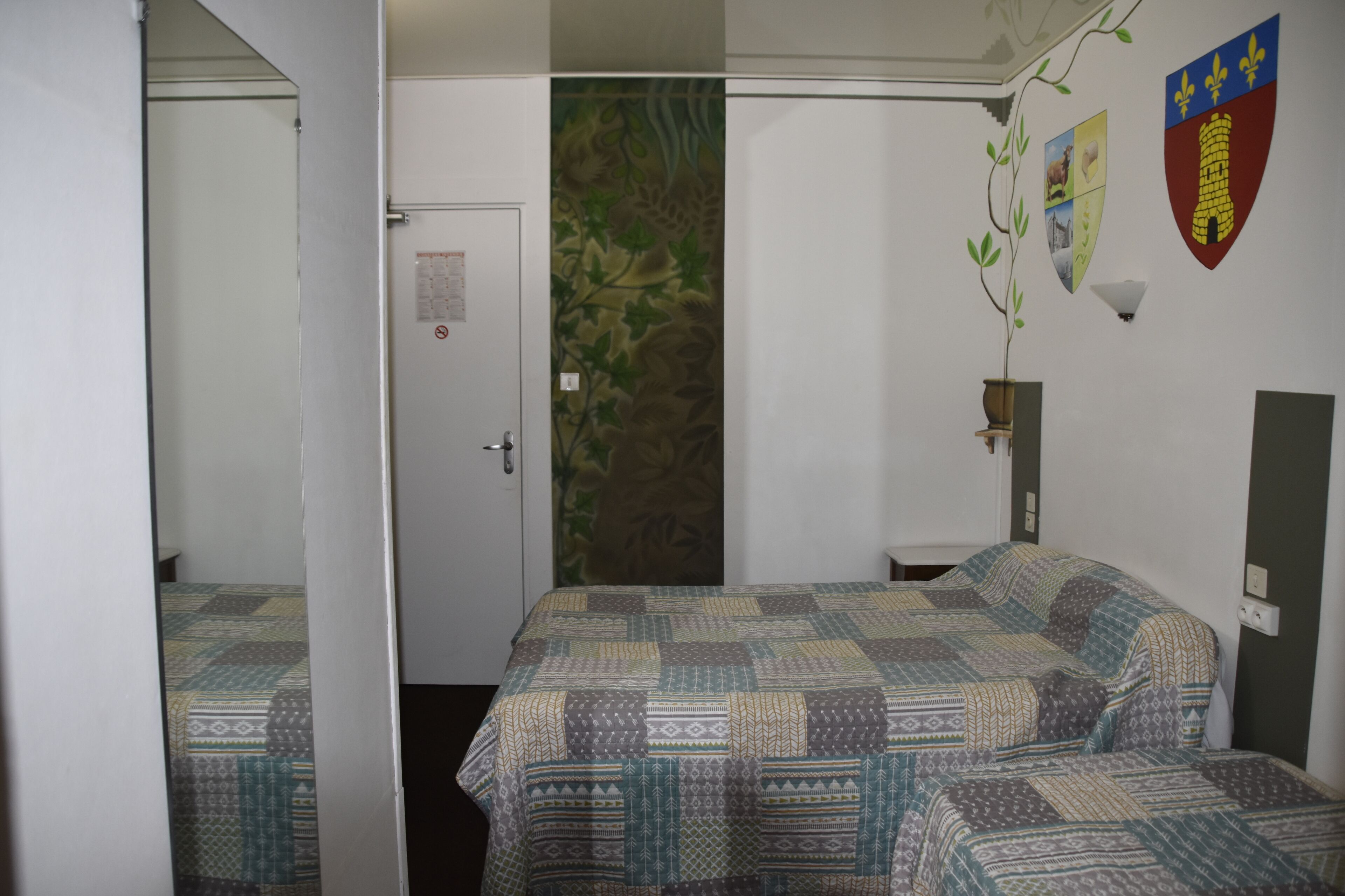Una habitación con dos camas, una puerta, una pared con estampado floral y un escudo en la pared.