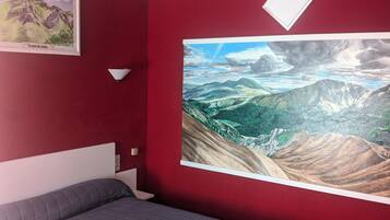 A bedroom with a bed, a large landscape painting on the wall, and a framed picture above the bed.