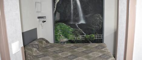 Un dormitorio con cama, un interruptor de luz en la pared y un cartel grande de una cascada.