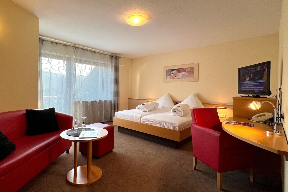 A hotel room with a bed, a red sofa, a small round table, and a TV.