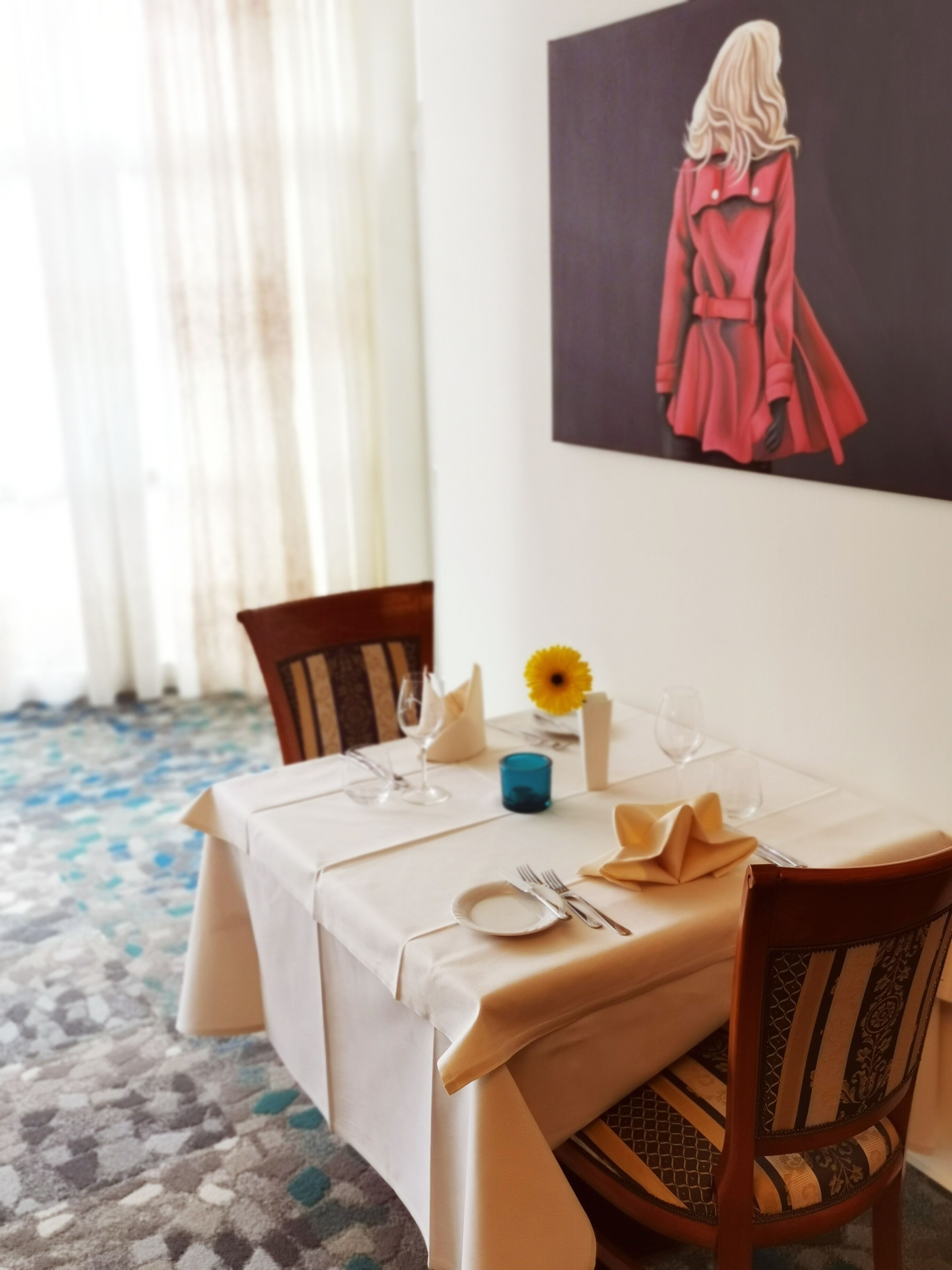 A dining table set with a white tablecloth, a vase with a yellow flower, and a blue candle holder.