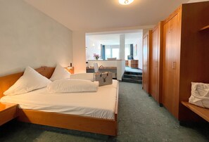 Quarto de hotel com cama de madeira, uma mesa com cadeira e vista para o corredor e outro quarto.