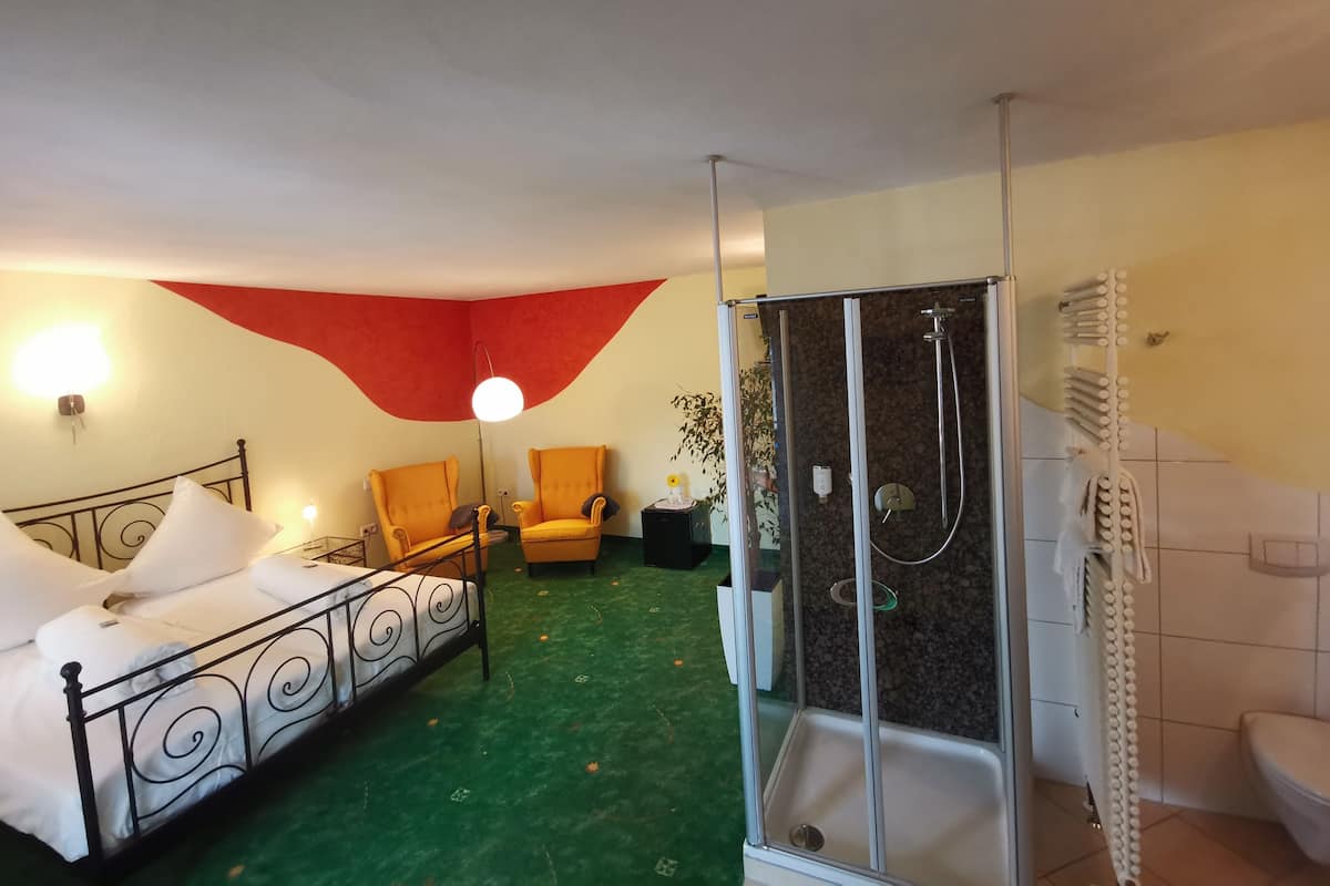 A hotel room with a bed, a chair, a shower, and a toilet.