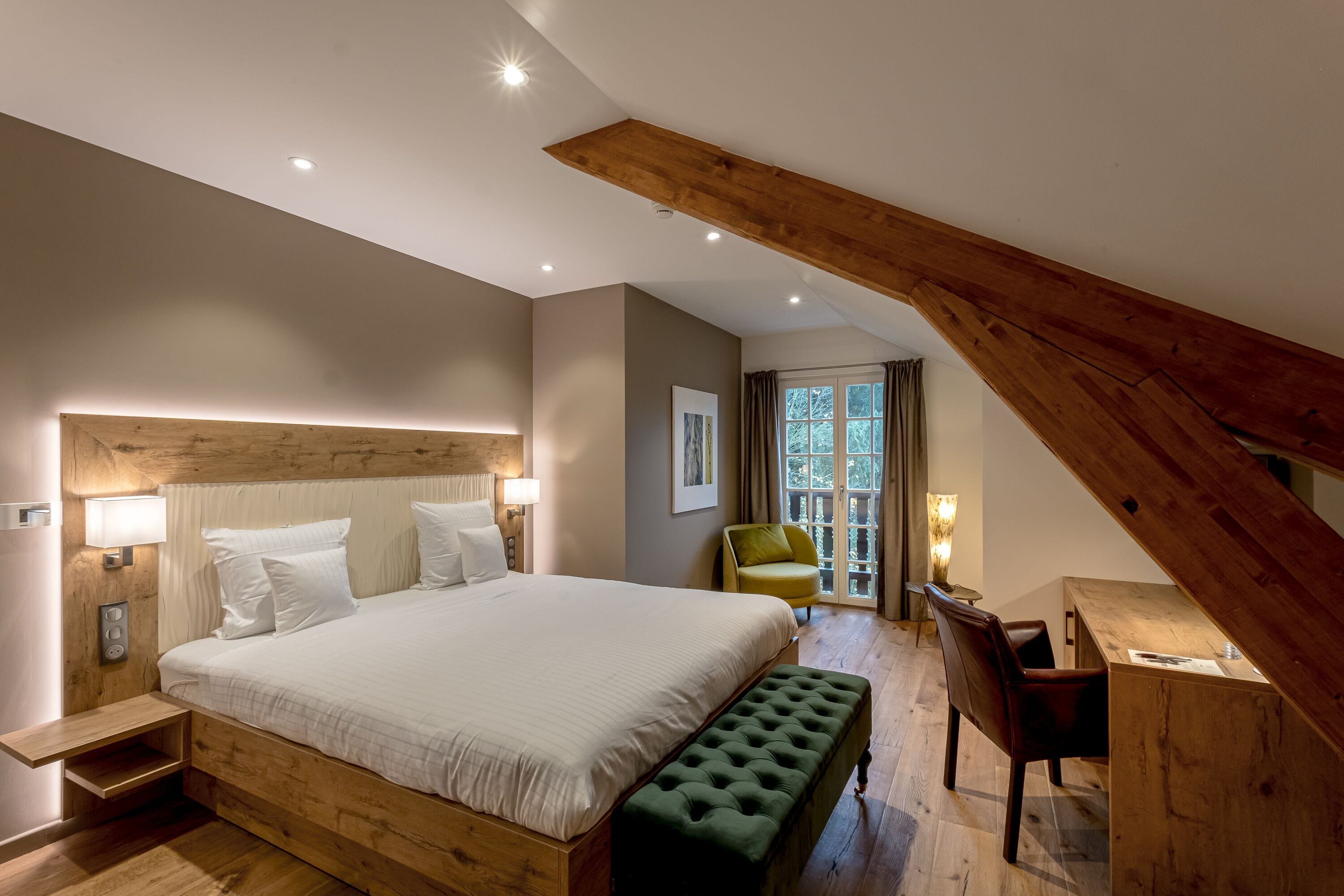 Une chambre avec un grand lit, un bureau en bois et un banc vert.