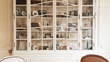 Una habitación con un amplio ventanal de arco que muestra diversos objetos decorativos. Hay una mesa redonda con dos sillas frente al ventanal.