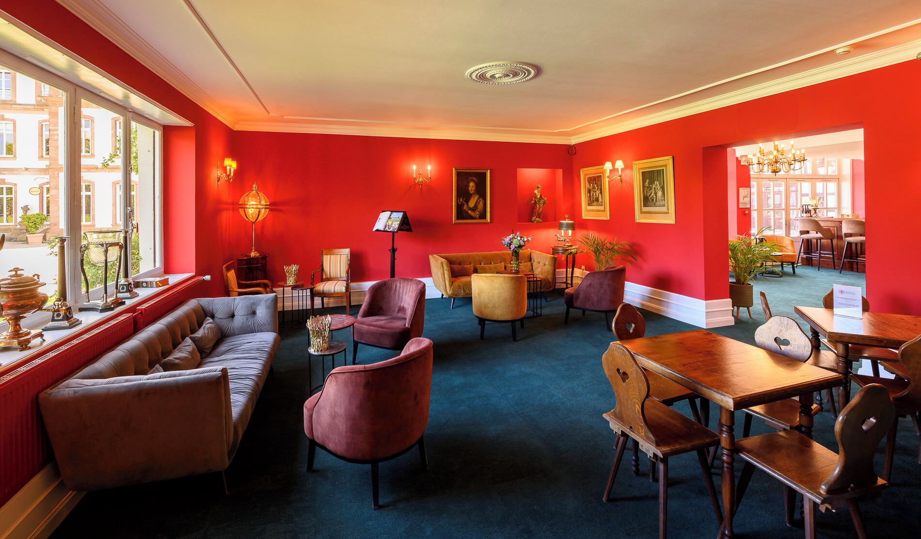 Un hall d’hôtel avec un mur rouge, un canapé, des fauteuils, une table et un lustre.
