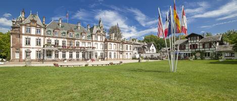 A historic building with a large lawn in front, multiple flags, and a well-maintained garden.