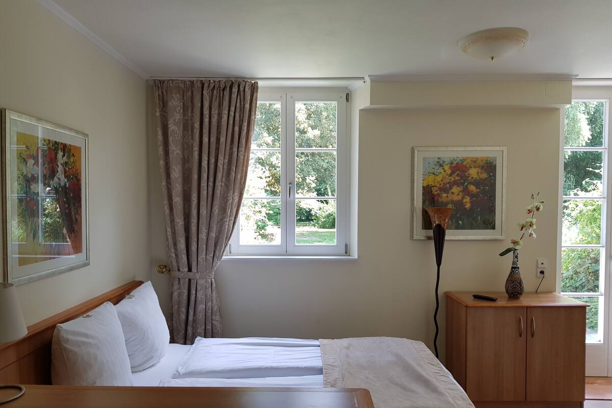 A bedroom with a bed, a window with curtains, a cabinet, and two paintings.