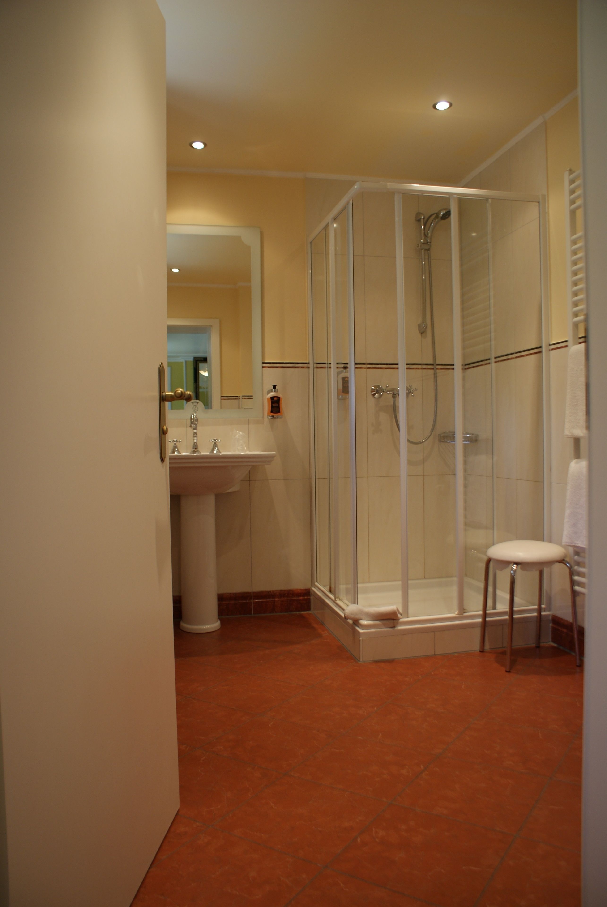 A bathroom with a glass-enclosed shower, a sink, and a white chair.