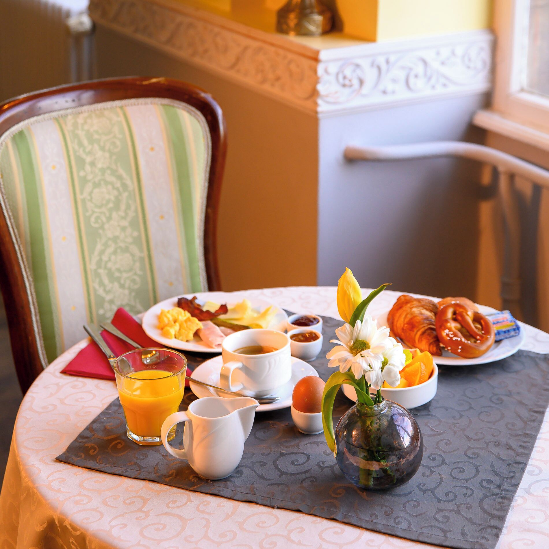 Une table de petit-déjeuner avec une assiette d’œufs, de bacon, des croissants et un verre de jus d’orange.