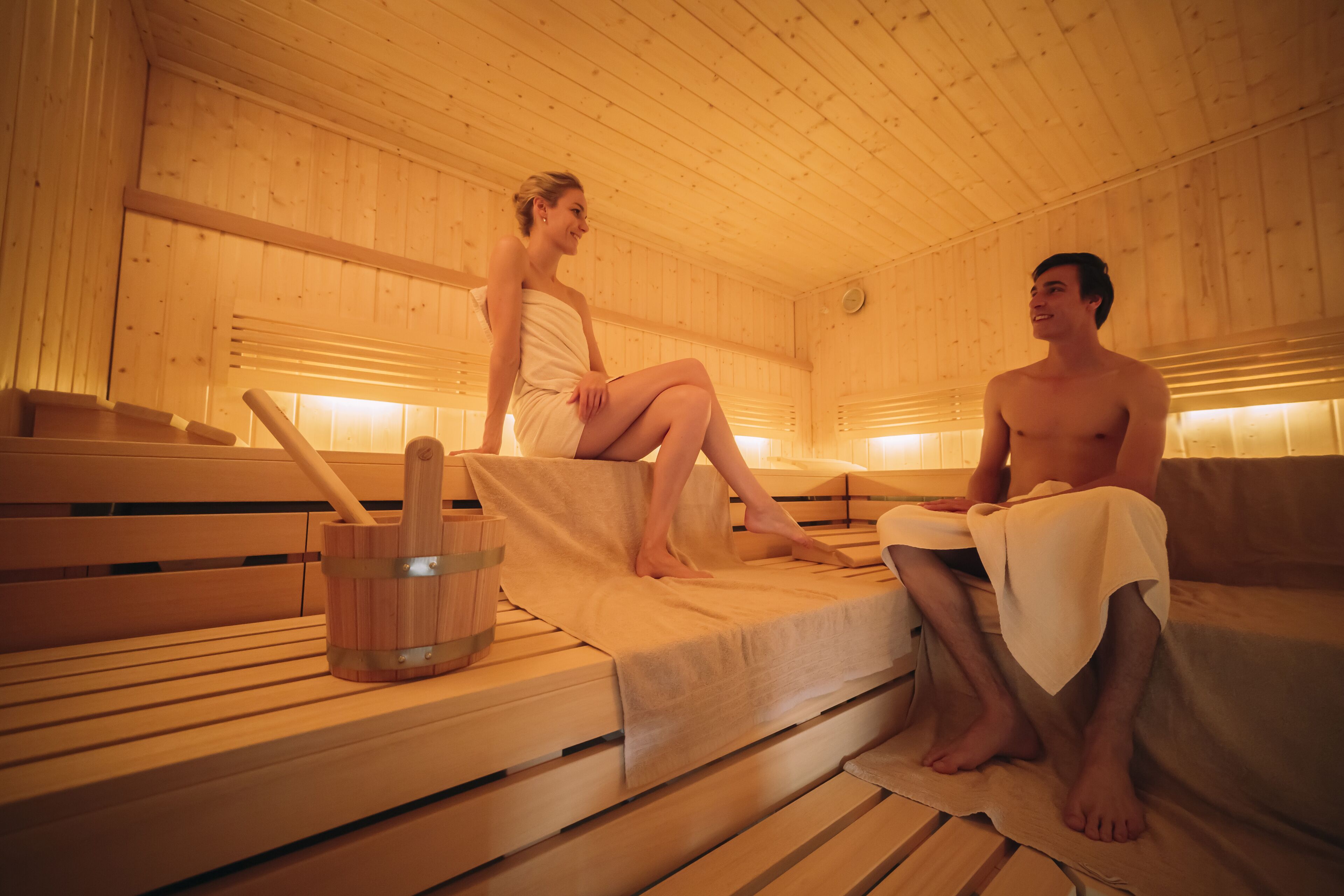 A sauna with wooden benches and benches, a wooden bucket, and a towel.