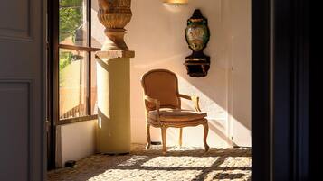 A stone-floored room with a chair, a large vase, and a wall-mounted light fixture.