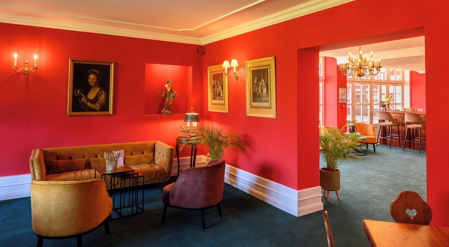 A red-walled room with a sofa, chairs, a table, and a chandelier.