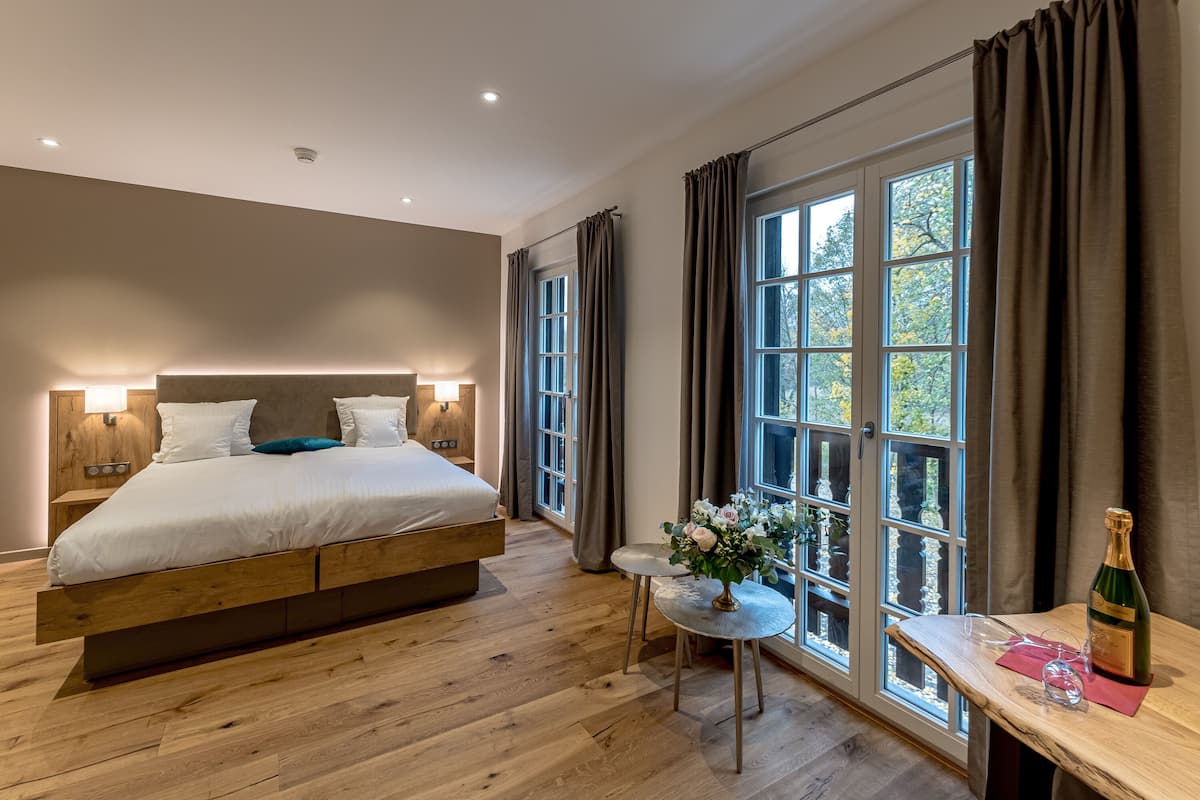 A modern bedroom with a large bed, a small table with a vase, and a bottle of champagne.