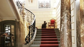 Una imponente escalera con alfombra roja, barandales de metal ornamentados y columnas de mármol.