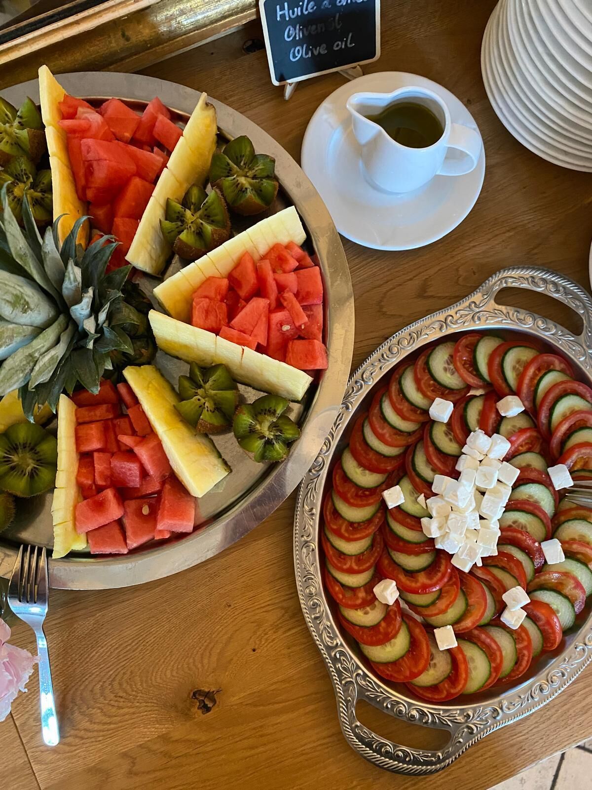 A table with a fruit platter, a vegetable tart, a cup of olive oil, and a sign indicating the oil's origin.