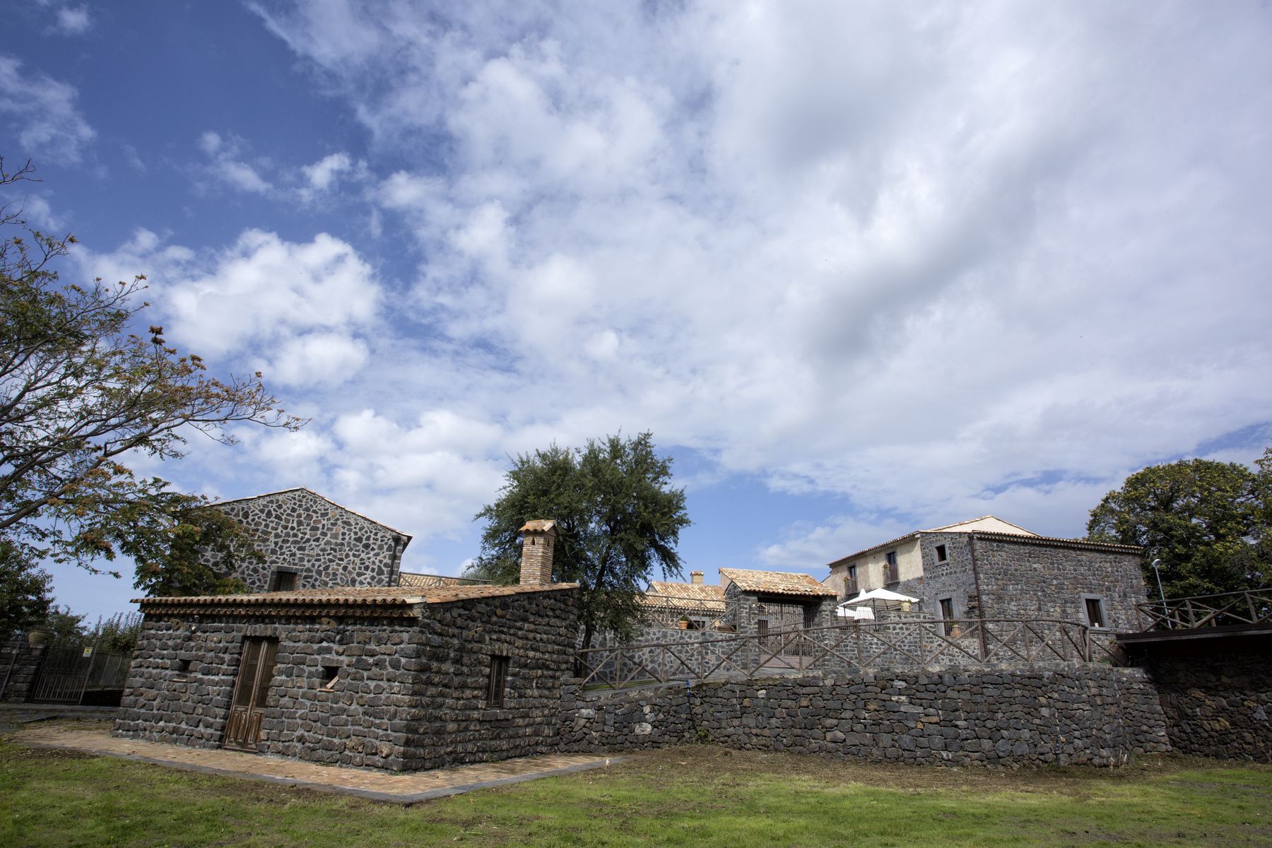 A stone building with a tiled roof, surrounded by trees and a clear sky.