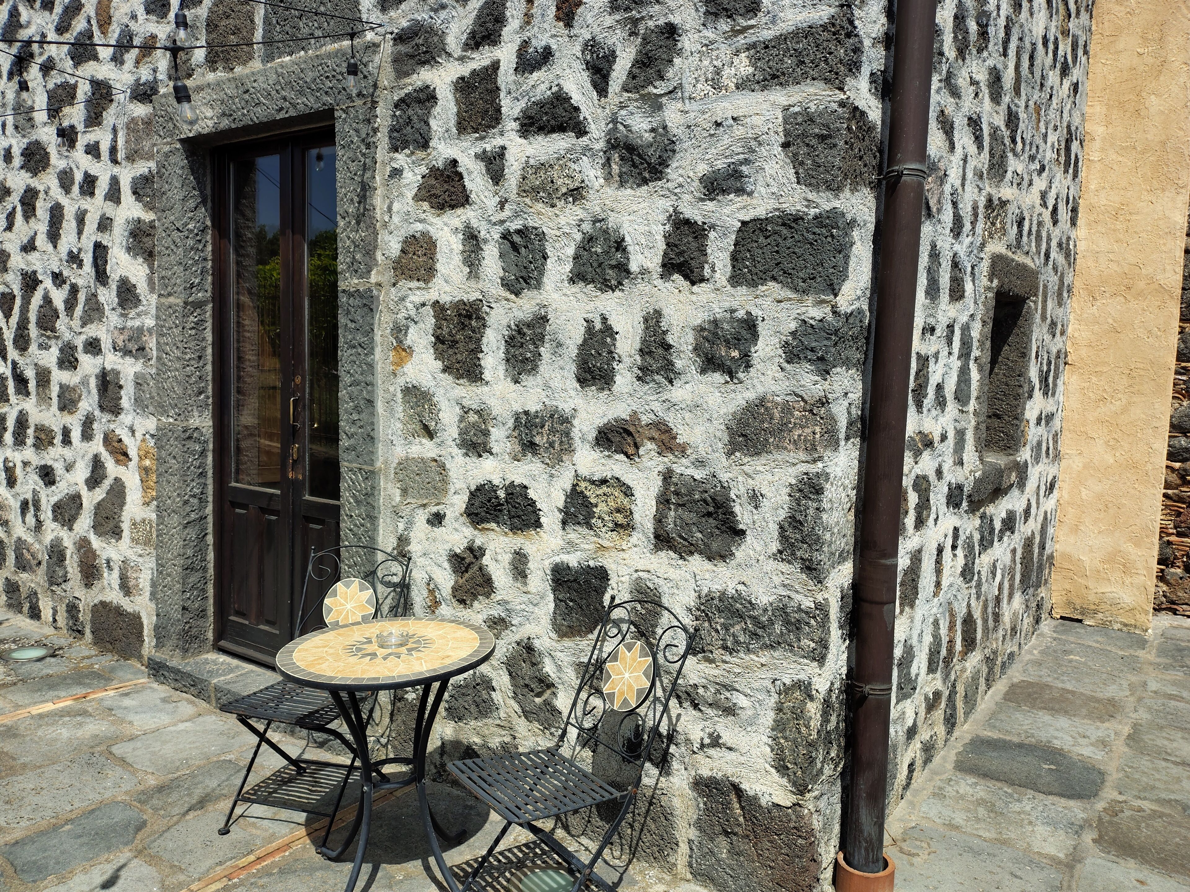 Ein Steinhaus mit einer Tür und einer kleinen Außenbereich-Sitzgelegenheit mit Tisch und Stühlen.