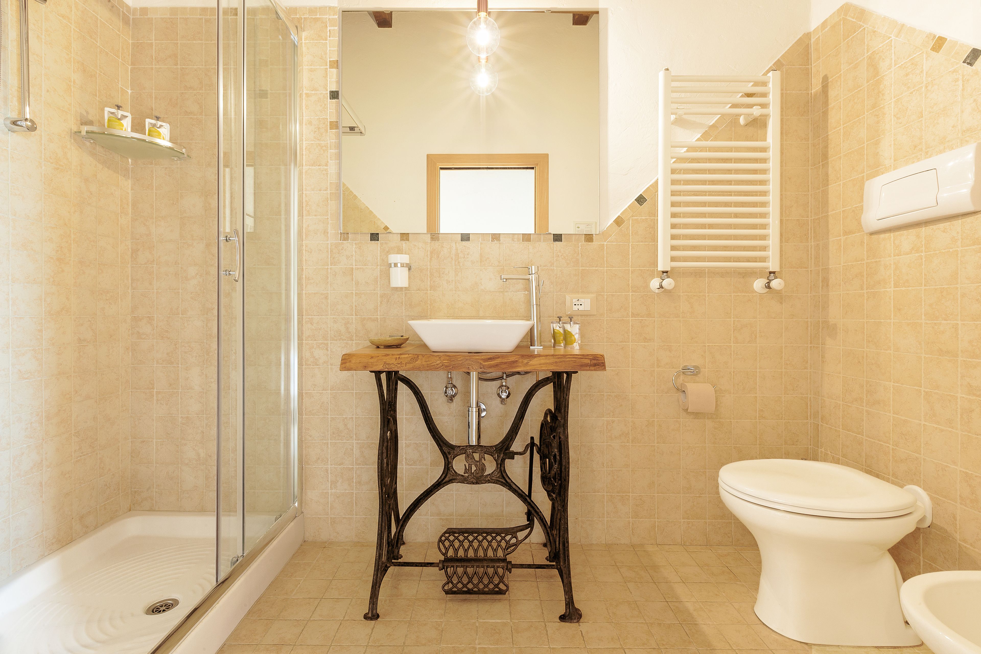 A bathroom with a glass shower enclosure, a sink with a wooden countertop, a toilet, and a mirror above the sink.