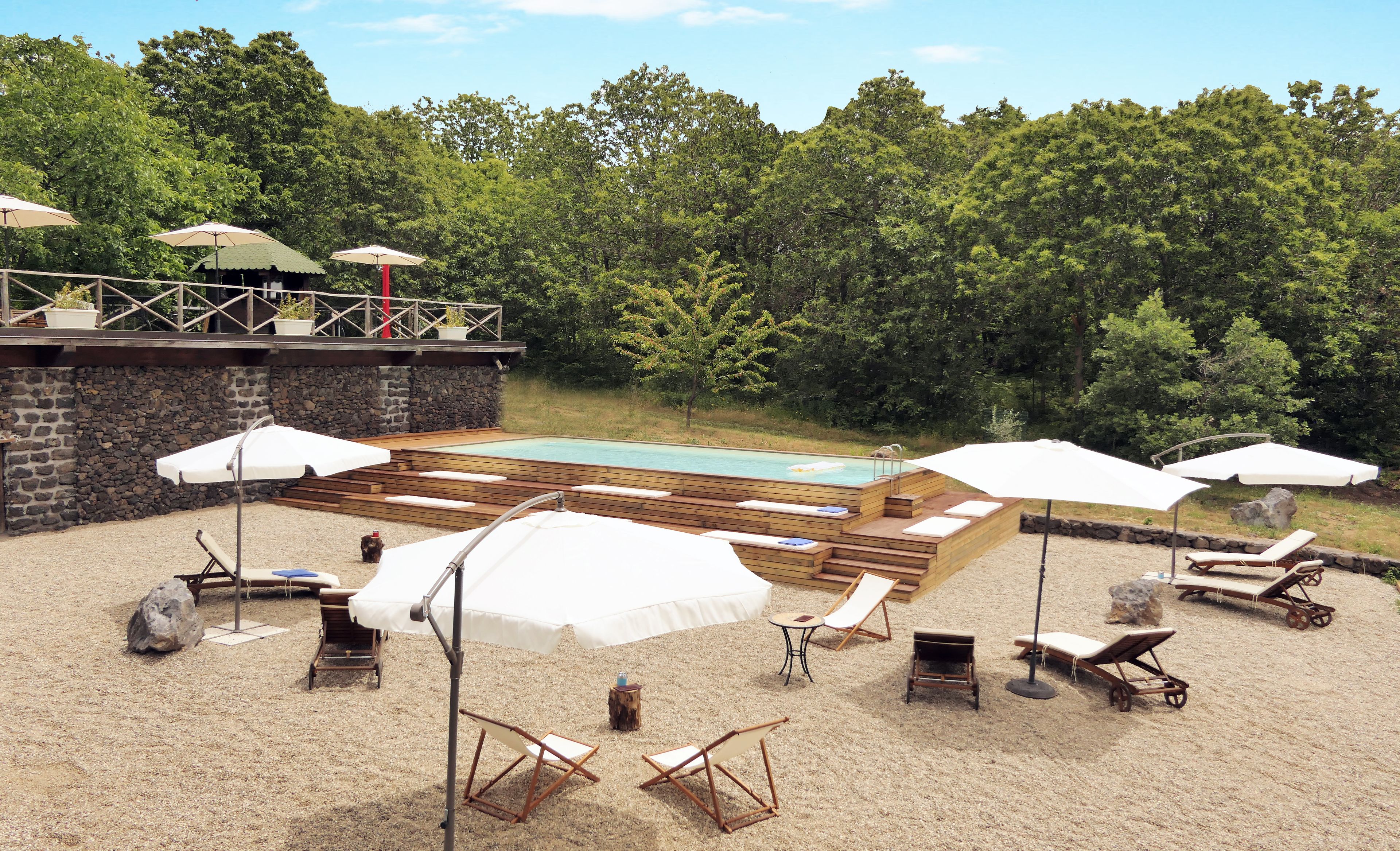 Un espace extérieur avec une piscine, des chaises longues, des parasols et une terrasse en bois.
