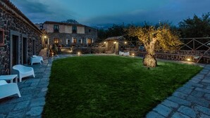A courtyard with stone buildings, a well-maintained lawn, outdoor seating, and a tree. - Bosco Ciancio (Biancavilla)