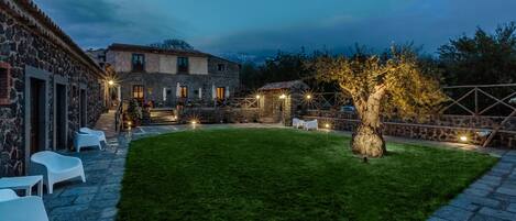 A courtyard with stone buildings, a well-maintained lawn, outdoor seating, and a tree.