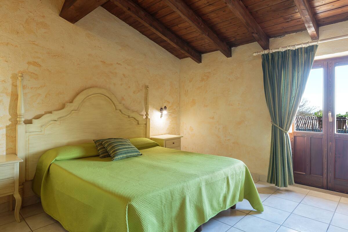 A bedroom with a bed, nightstand, and a window with curtains.