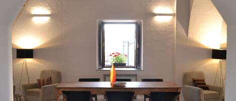 A dining area with a wooden table, four chairs, a red patterned rug, and two wall-mounted lamps.