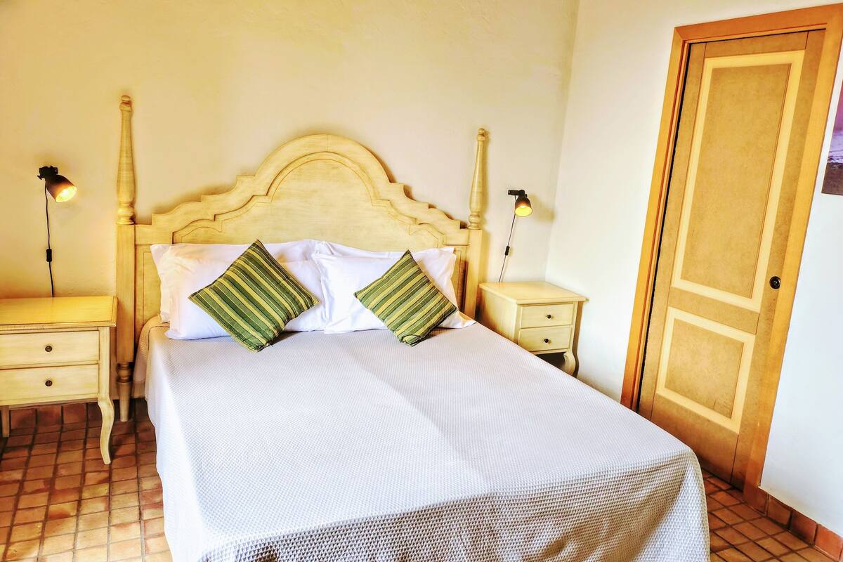 A neatly made bed with a wooden headboard, two bedside tables with lamps, and a door to the right.