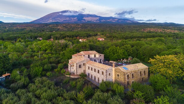 A stone building with a flat roof surrounded by dense greenery and a mountain in the background. - Bosco Ciancio (Biancavilla)