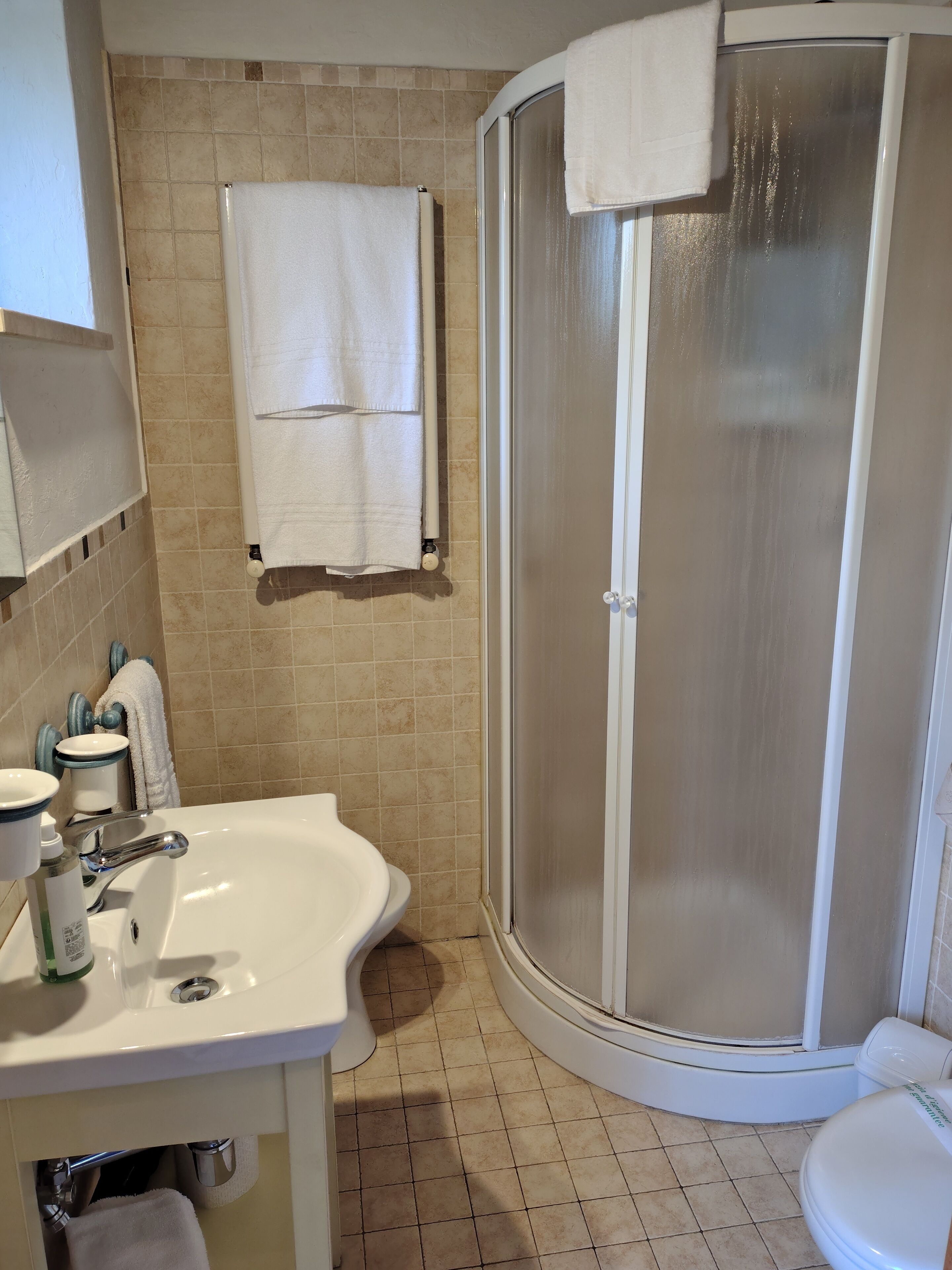 A bathroom with a white sink, mirror, and toilet, a shower with a glass door, and beige tiled walls.