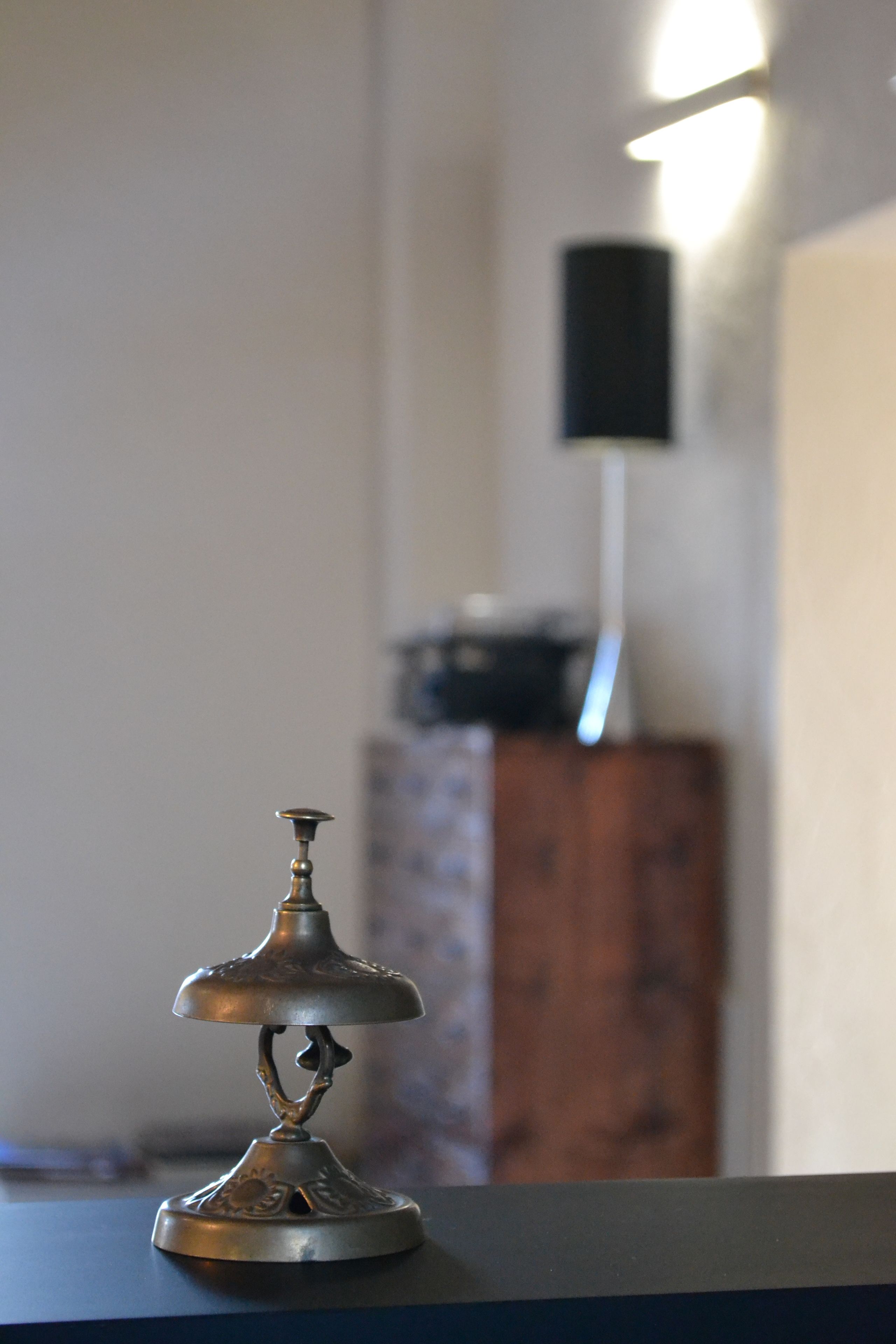 A small, ornate metal object on a dark surface, with a blurred background including a wooden cabinet and a wall-mounted speaker.