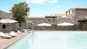 A pool area with stone walls, lounge chairs, and umbrellas. - Bosco Ciancio (Biancavilla)