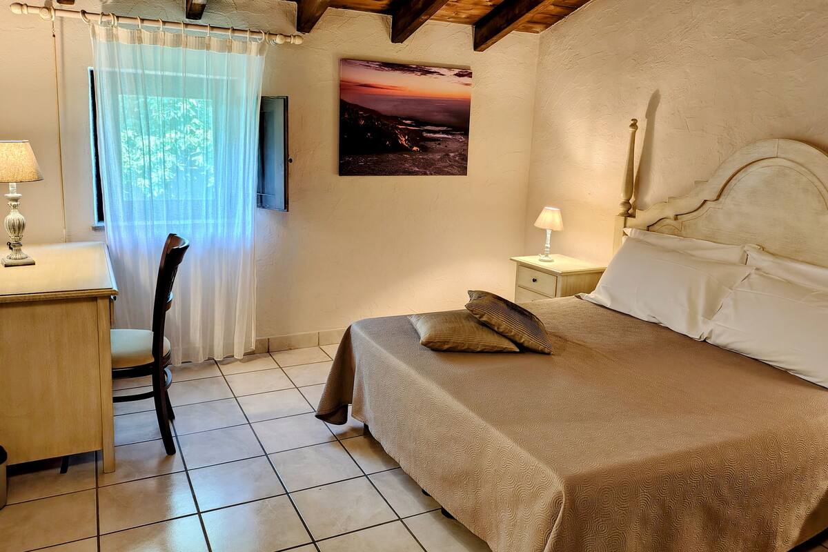 A bedroom with a bed, a nightstand, a chair, a desk, and a window with curtains.