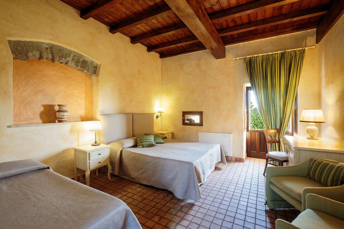 A room with two beds, a sofa, a small table, and a window with curtains.