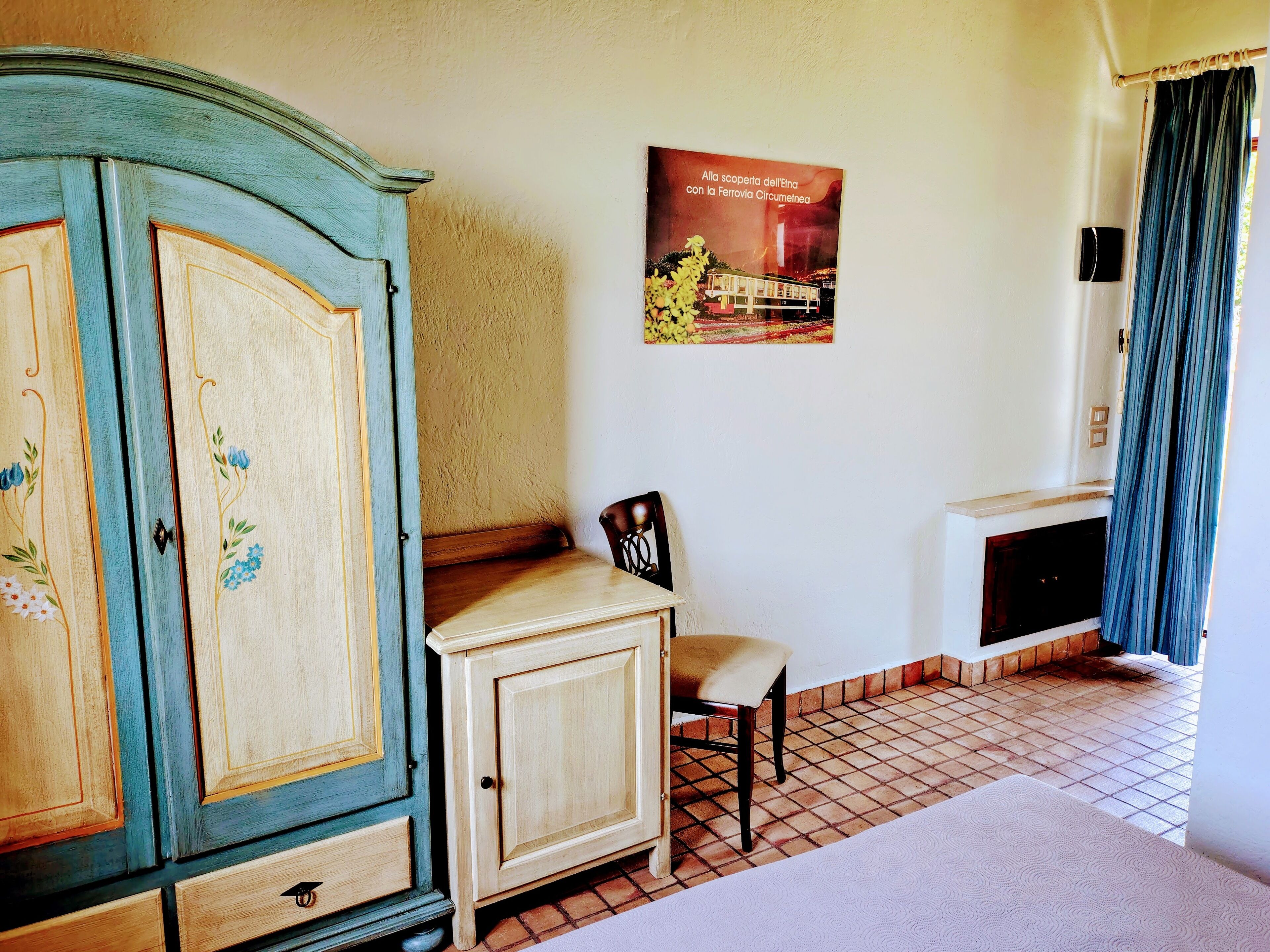 Une pièce comprenant un meuble en bois, une chaise, une petite table, une affiche accrochée au mur et une fenêtre avec des rideaux.