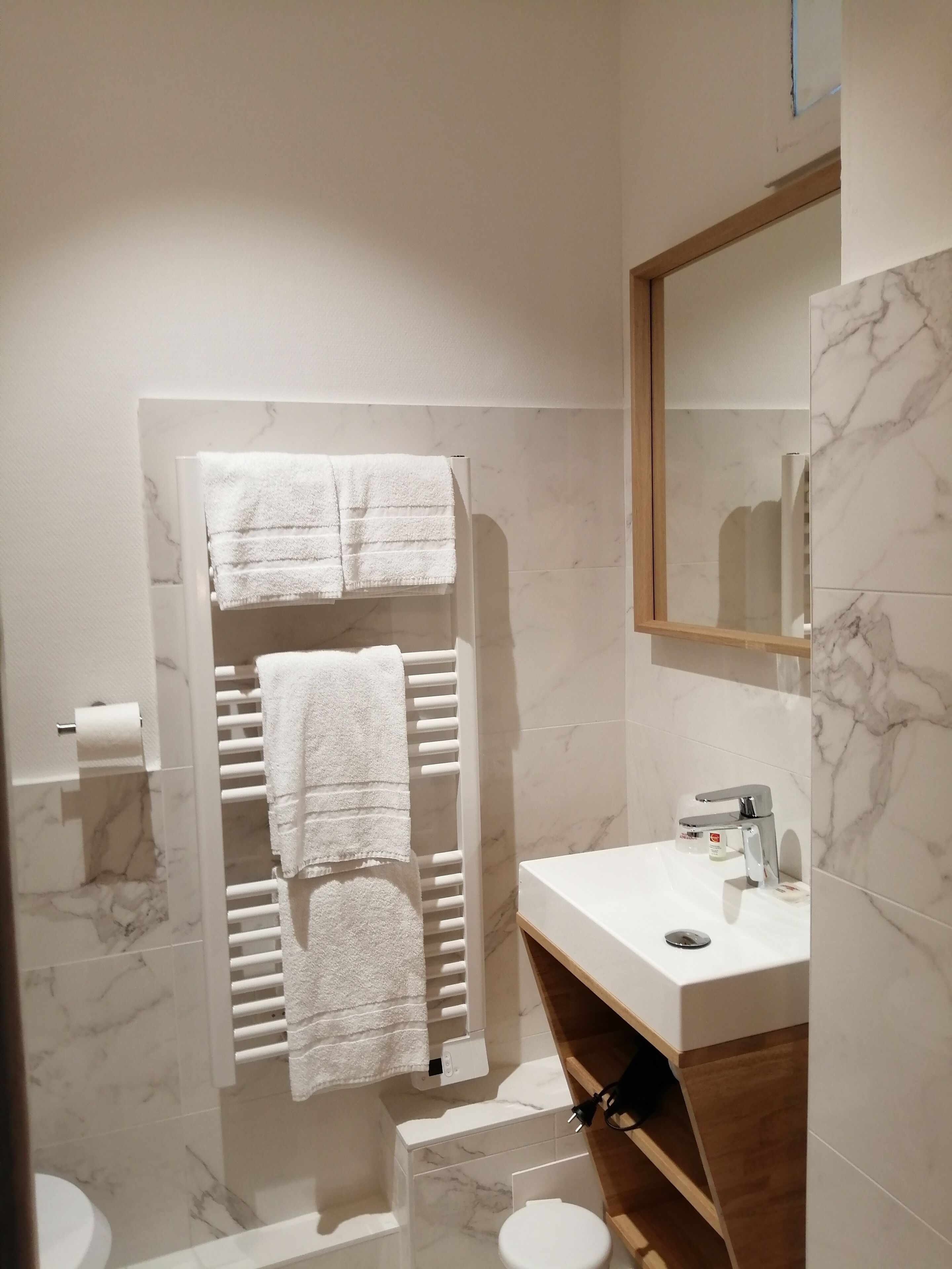 A modern bathroom with a white marble vanity, a towel rack with two towels, a toilet, and a shower area.