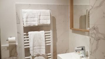 A modern bathroom with a white marble vanity, a towel rack with two towels, a toilet, and a shower area.