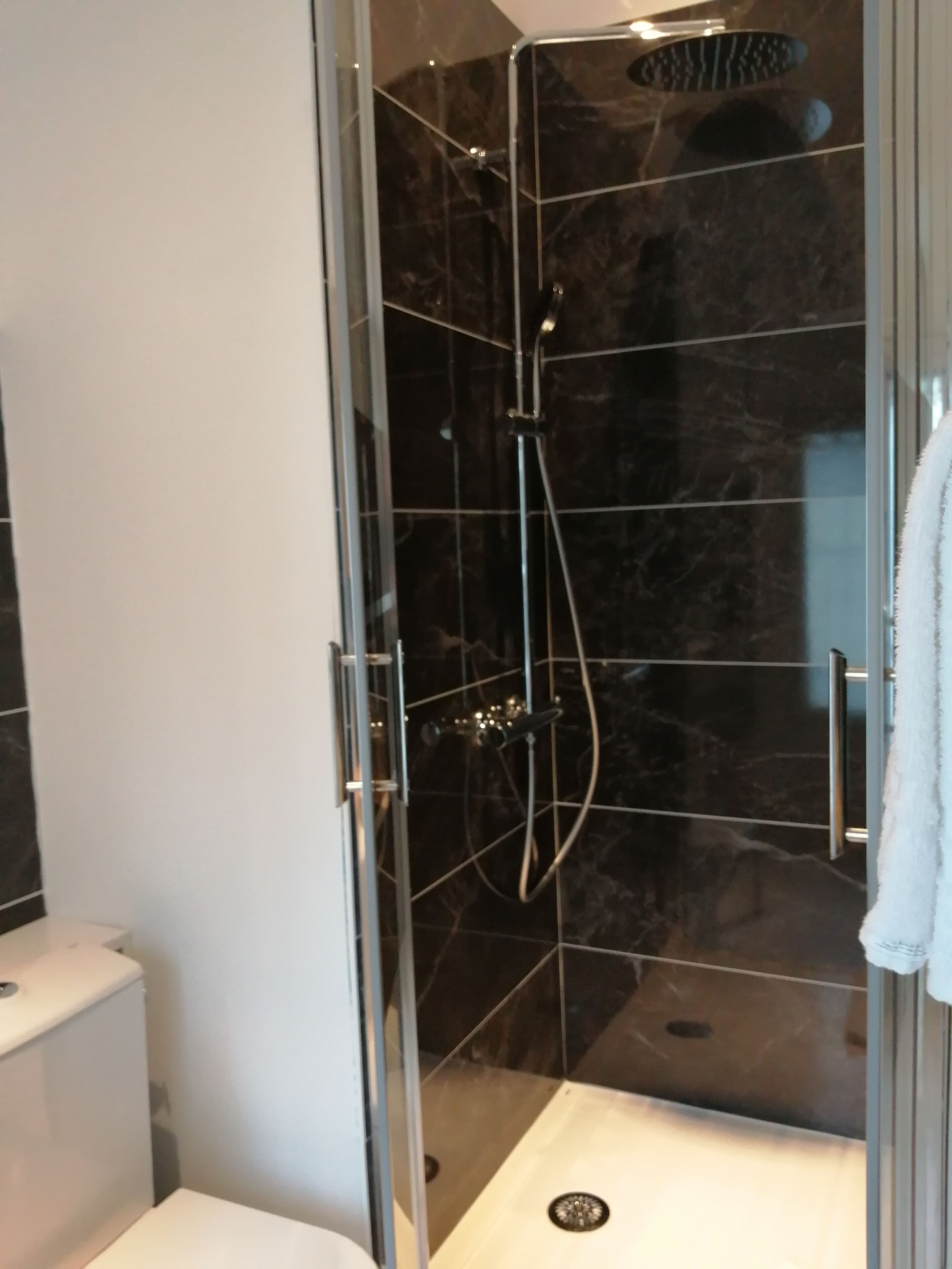A glass-enclosed shower with a handheld showerhead and a wall-mounted faucet.
