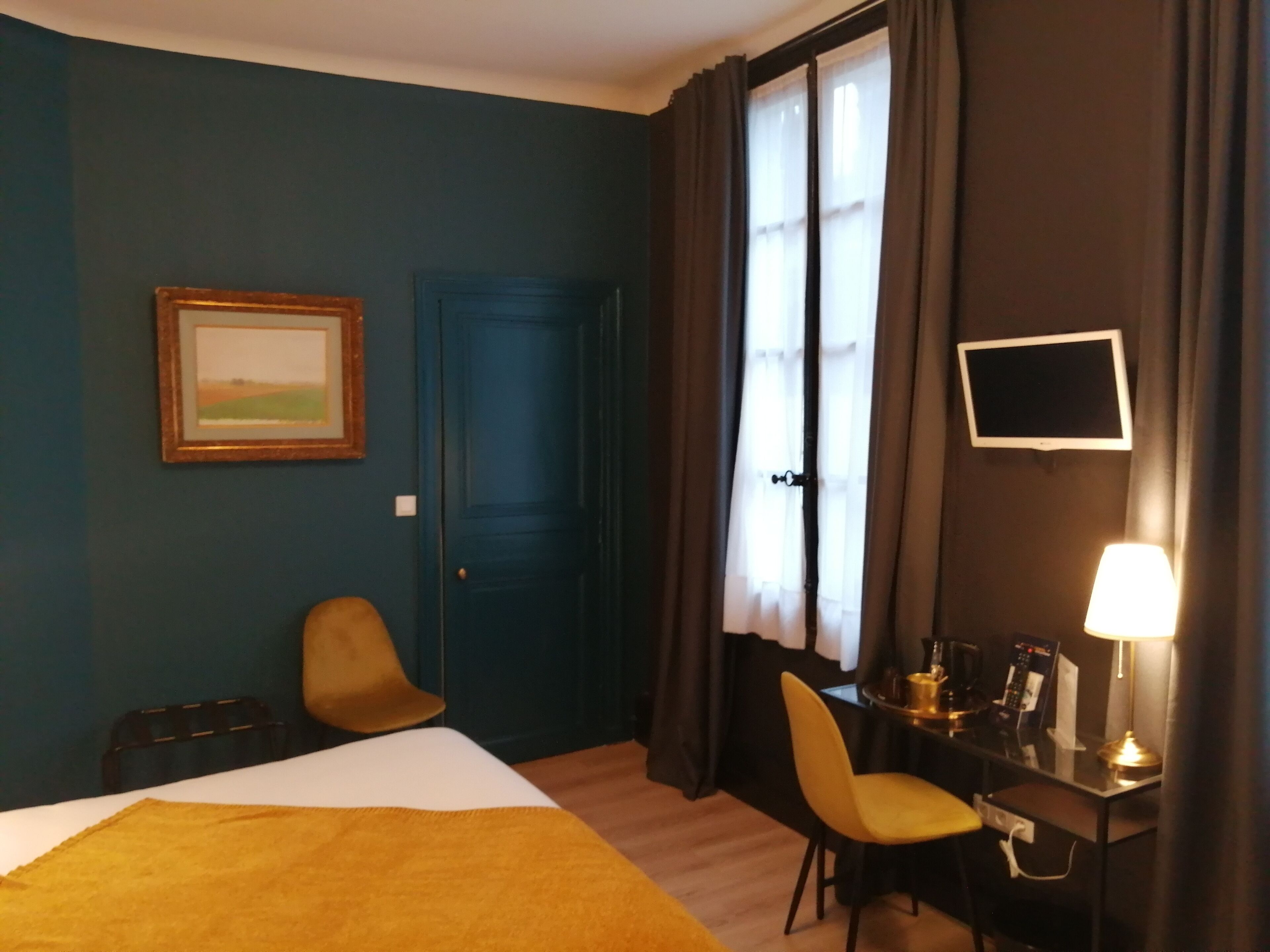 Una habitación de hotel con cama, escritorio con lámpara, silla, televisión y puerta.