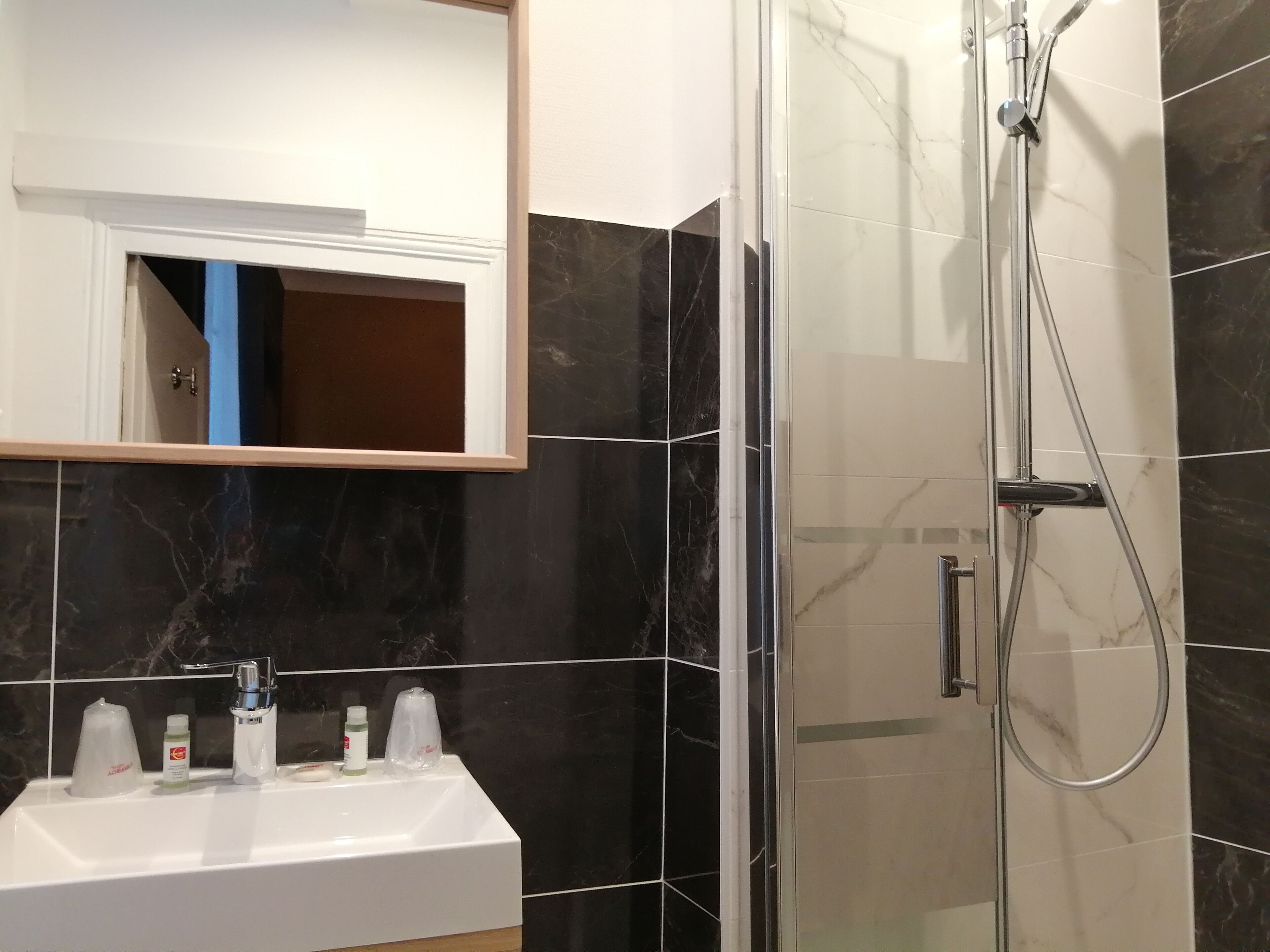Un baño con lavamanos blanco, un espejo y zona de ducha con mampara de cristal.