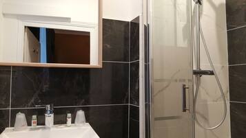 Un baño con lavamanos blanco, un espejo y zona de ducha con mampara de cristal.