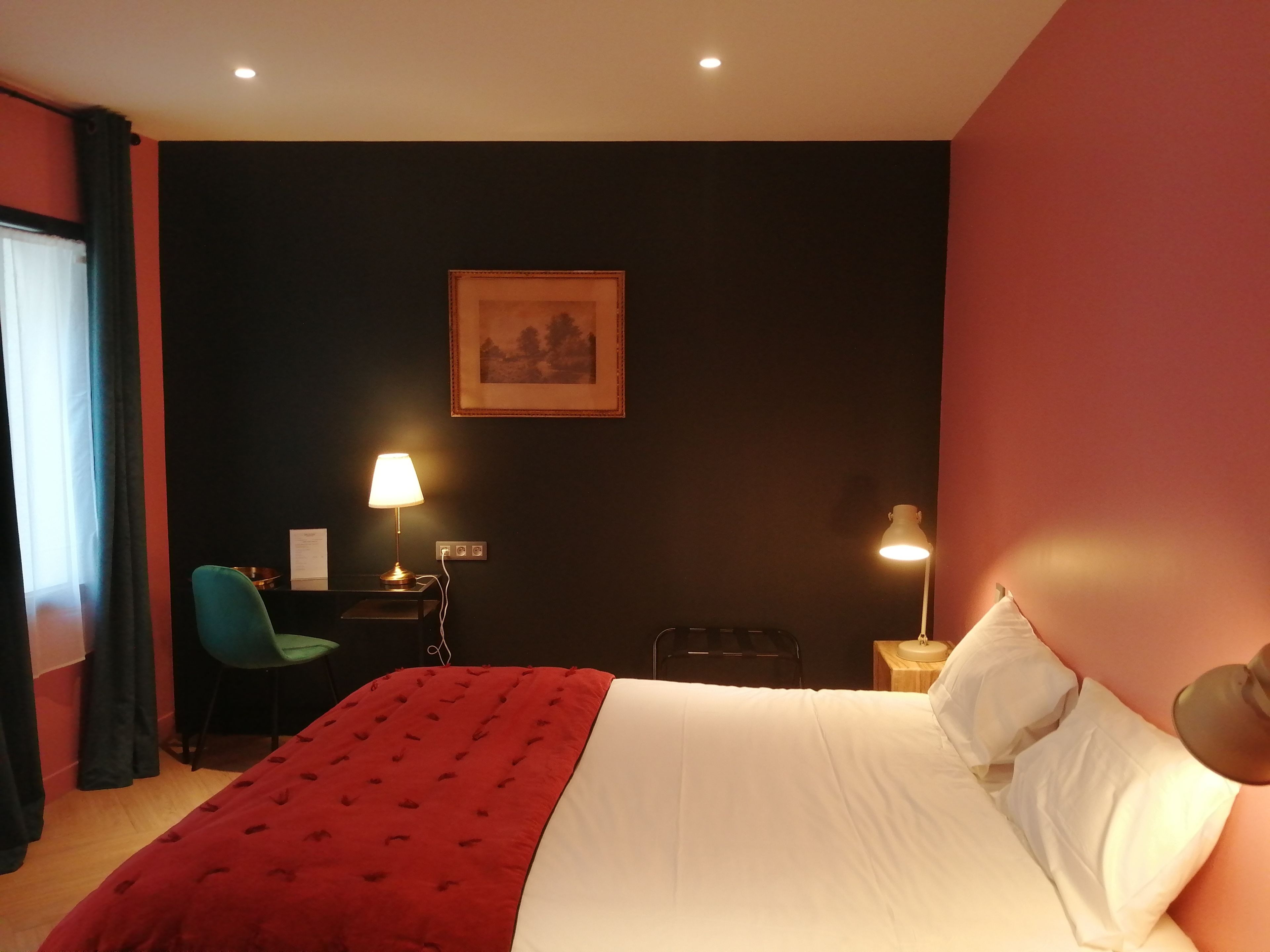 A hotel room with a bed, two bedside lamps, a chair, a desk, and a painting on the wall.