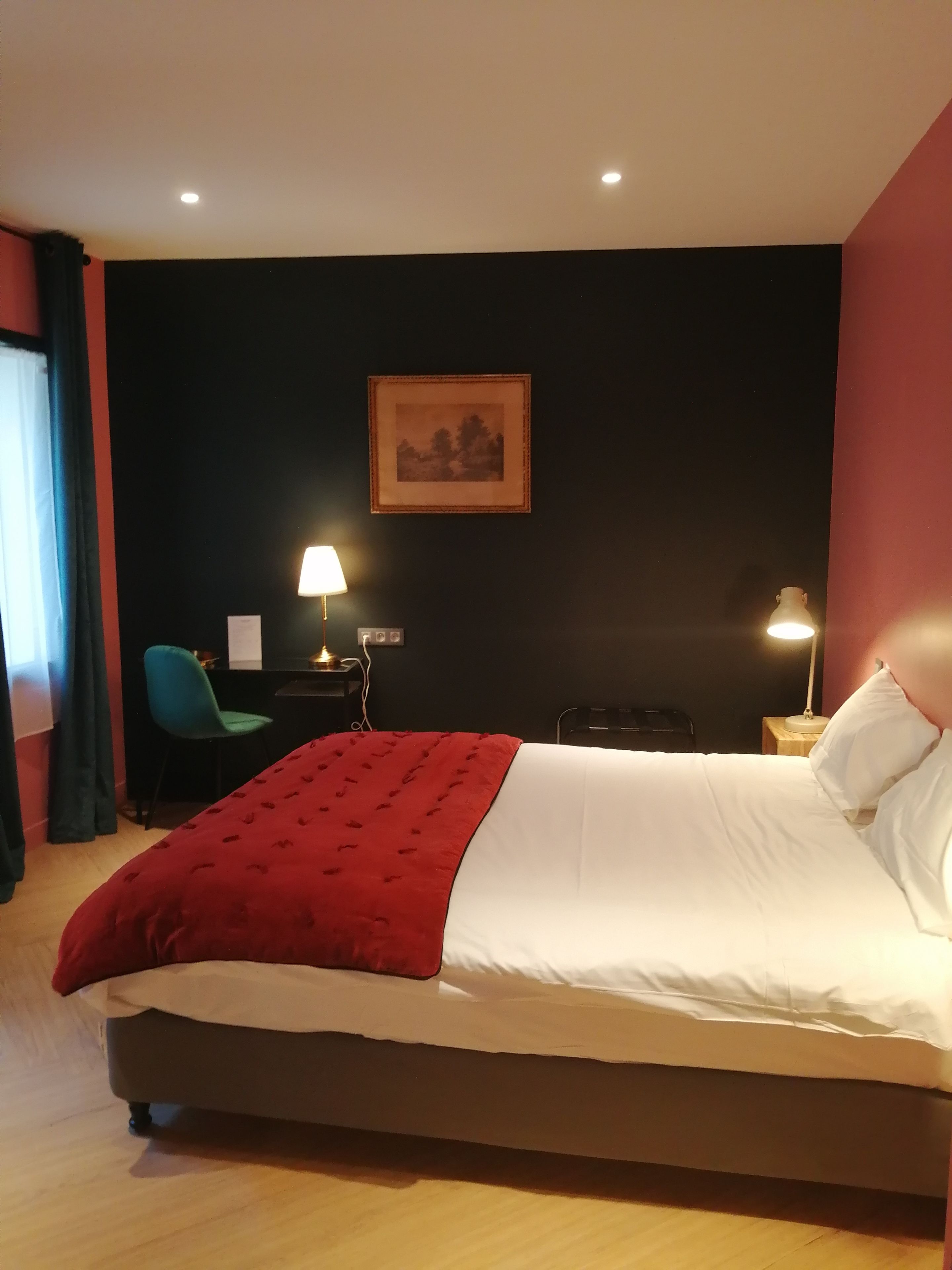 A hotel room with a large bed, a desk with a lamp, a chair, and a framed picture on the wall.