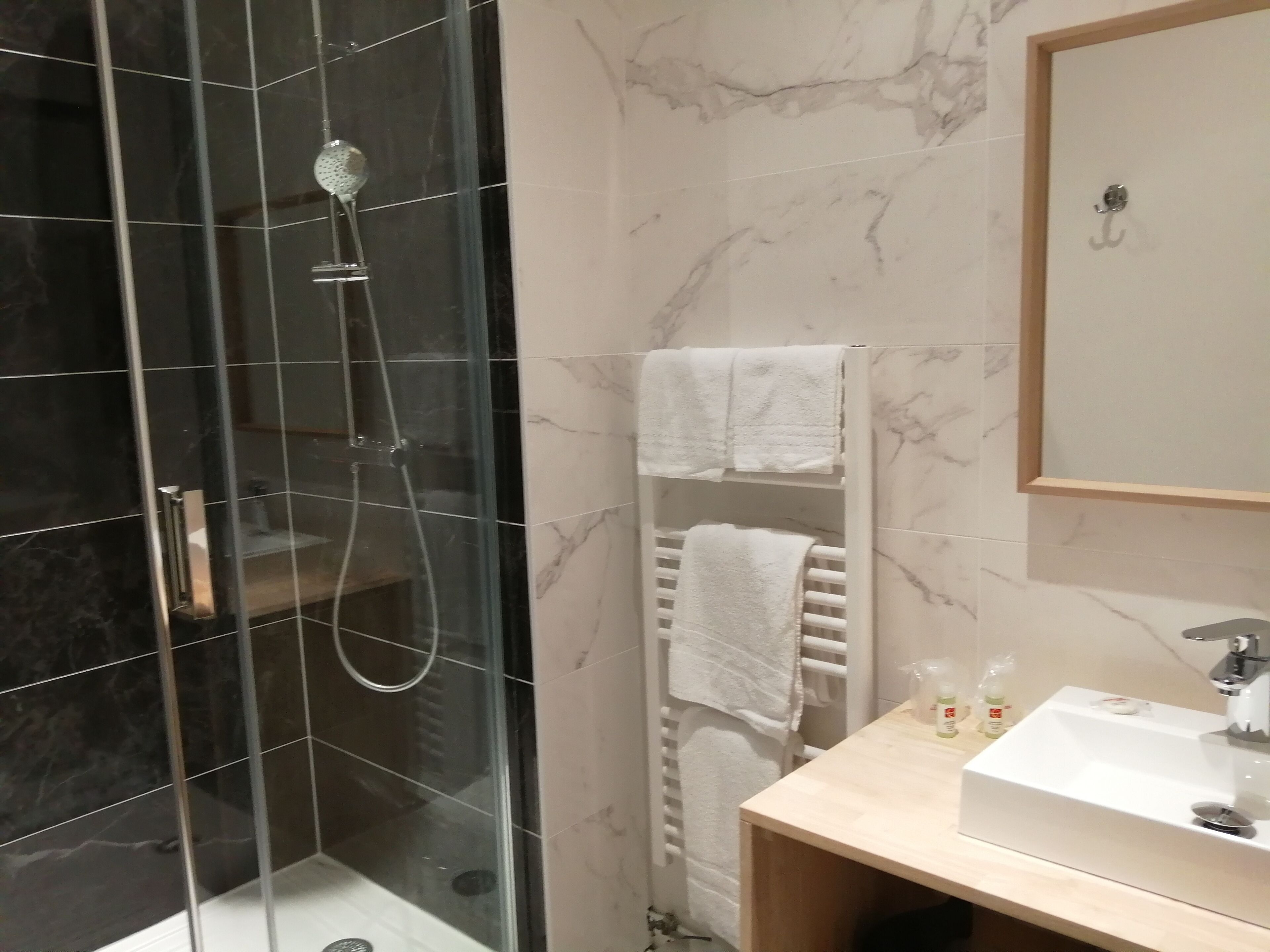 Un baño moderno con ducha de vidrio, lavabo blanco y un perchero para toallas.