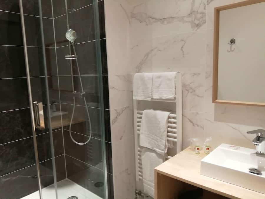 Un baño moderno con ducha de vidrio, lavabo blanco y un perchero para toallas.