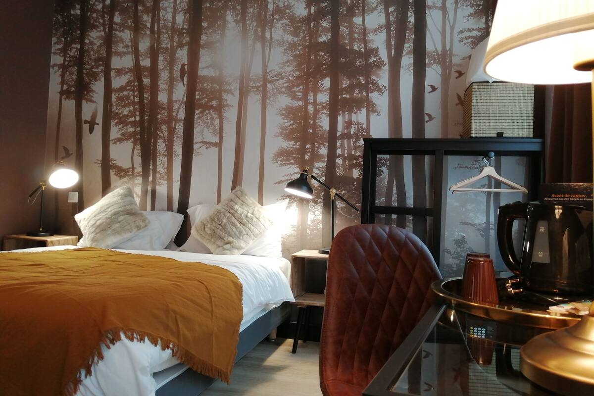 A hotel room with a bed, a chair, a desk, a lamp, and a coffee maker.