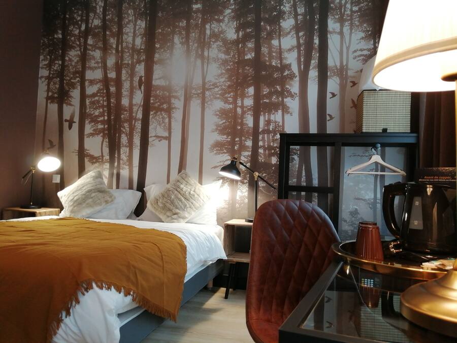 Quarto de hotel com cama, poltrona, escrivaninha, luminária e cafeteira.