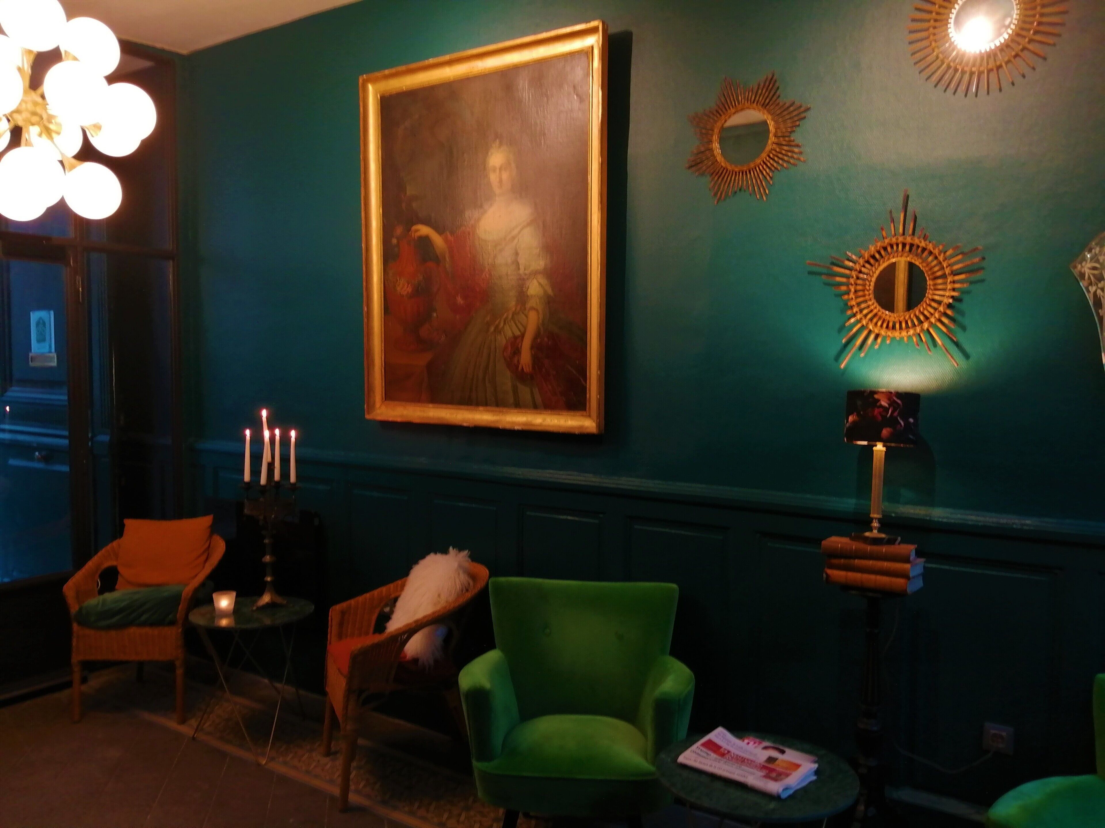 A room with teal walls, a large framed painting, a green armchair, a small table with a candle, and decorative wall mirrors.